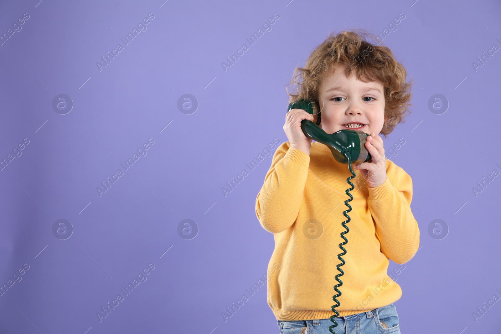 Photo of Cute little boy with telephone handset on violet background, space for text