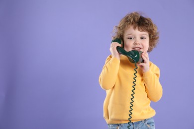 Photo of Cute little boy with telephone handset on violet background, space for text