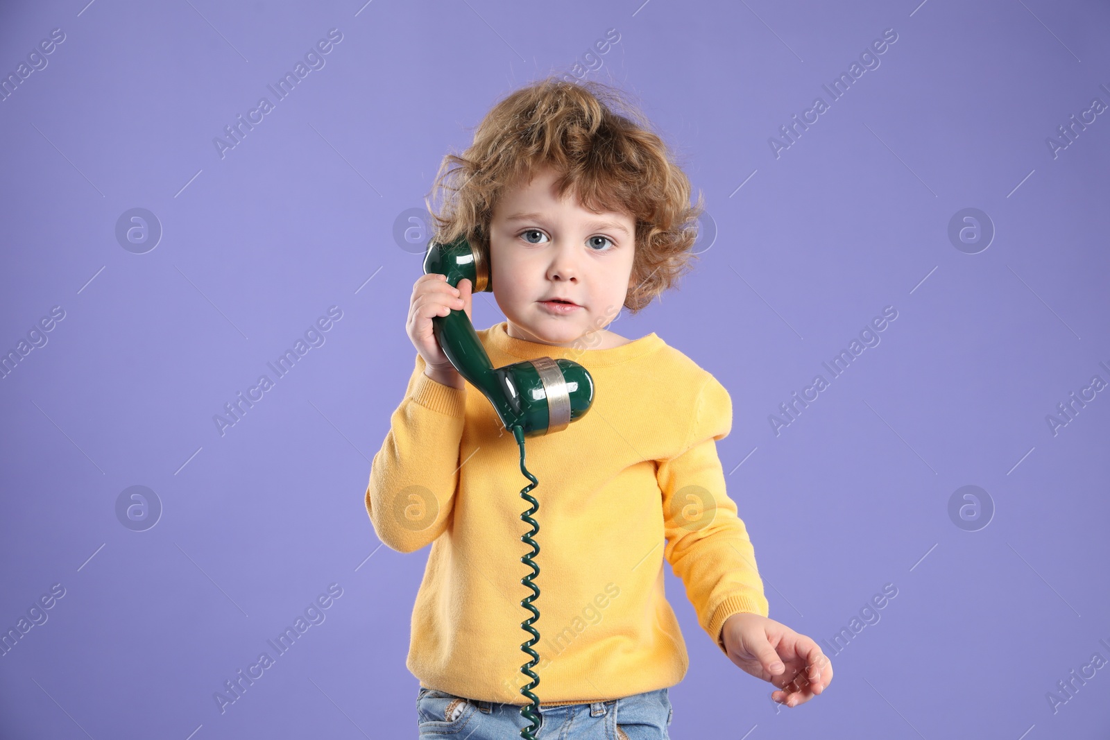 Photo of Cute little boy with telephone handset on violet background