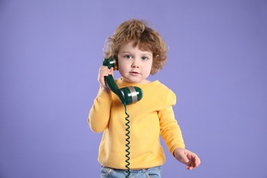 Photo of Cute little boy with telephone handset on violet background