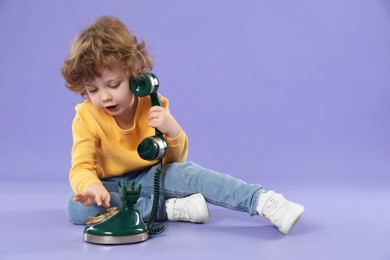 Cute little boy with old telephone on violet background