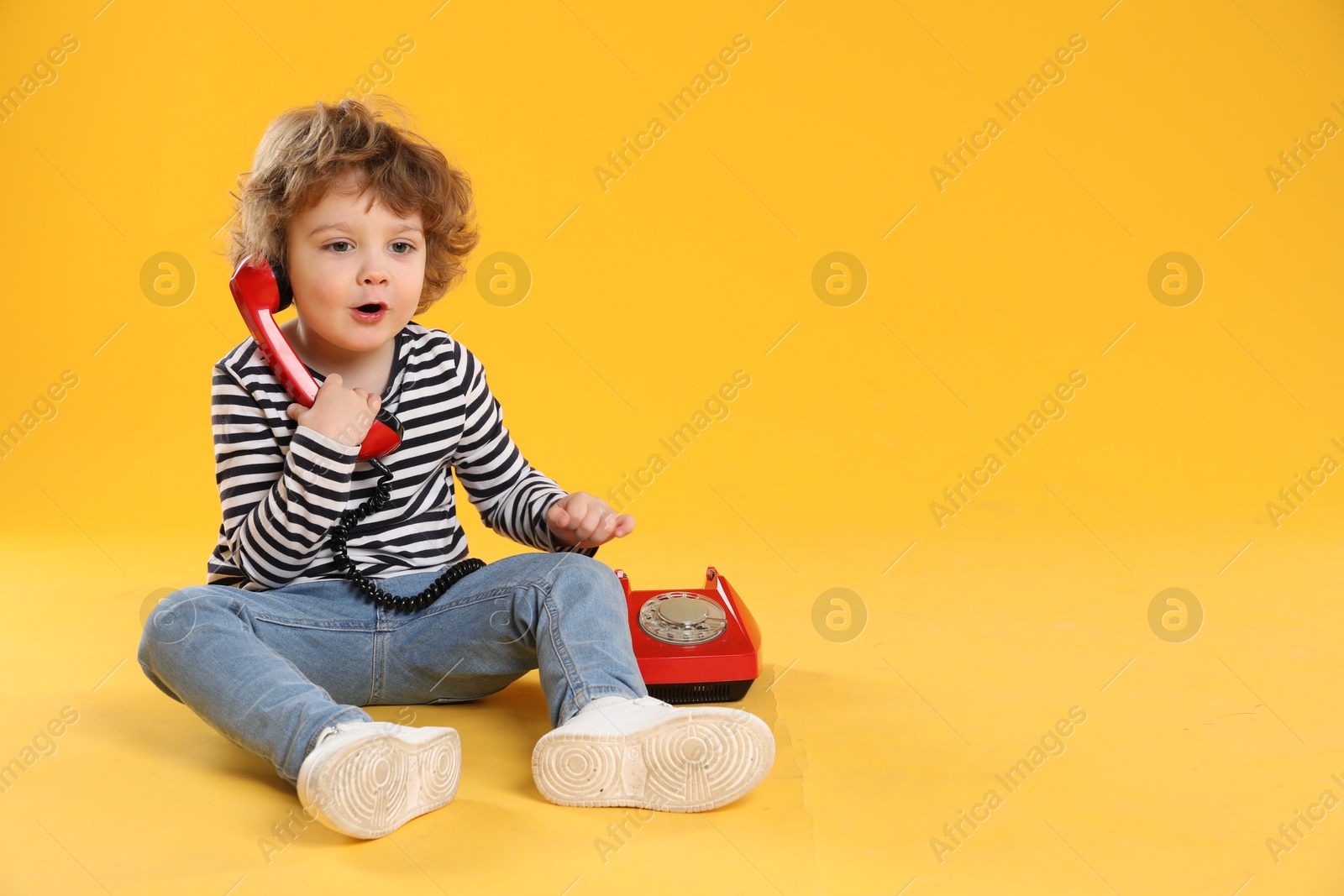 Photo of Cute little boy with telephone on orange background, space for text