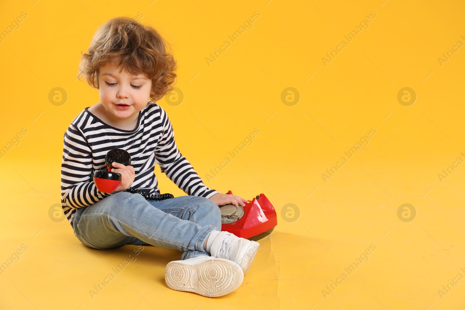 Photo of Cute little boy with telephone on orange background, space for text