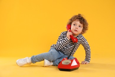 Photo of Cute little boy with telephone on orange background