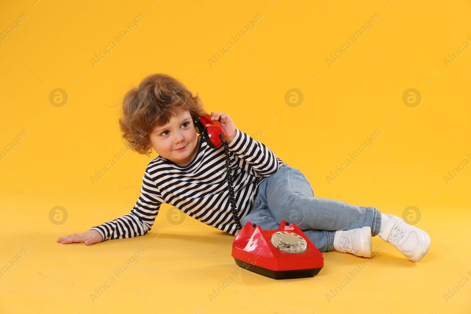 Photo of Cute little boy with telephone on orange background