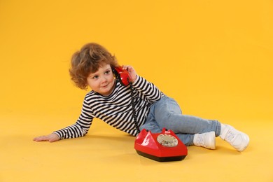 Photo of Cute little boy with telephone on orange background