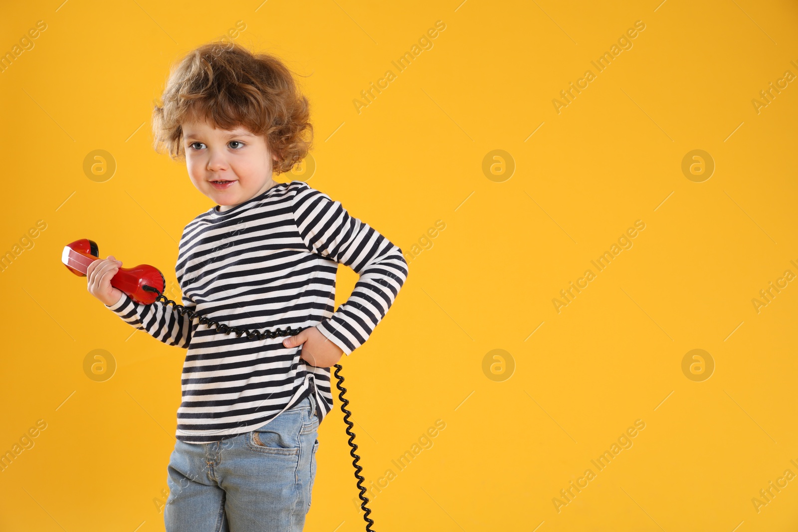 Photo of Cute little boy with telephone handset on orange background, space for text