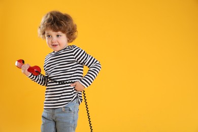 Photo of Cute little boy with telephone handset on orange background, space for text