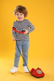 Photo of Cute little boy with telephone on orange background