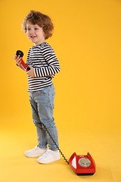 Photo of Cute little boy with telephone on orange background