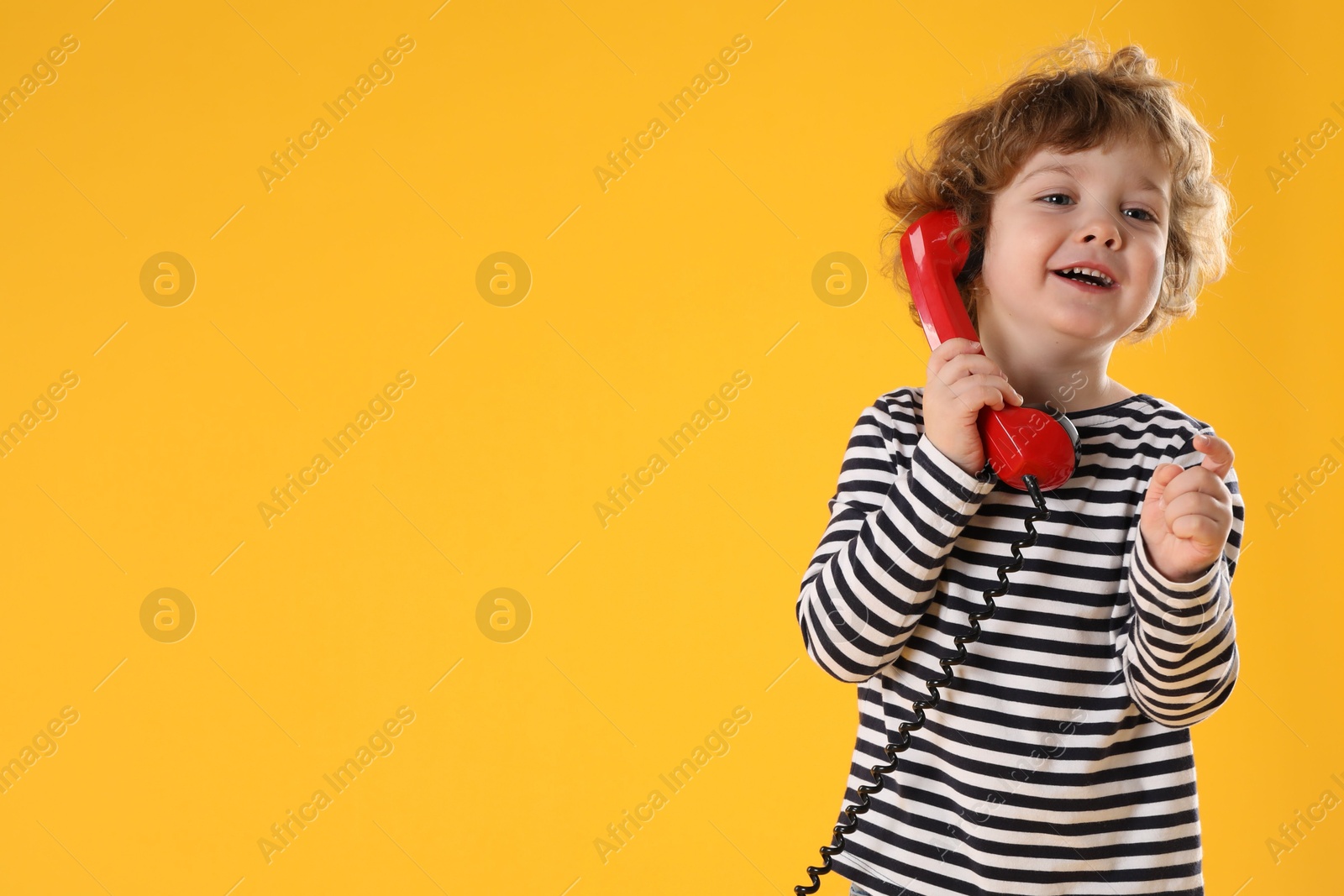 Photo of Cute little boy with telephone handset on orange background, space for text