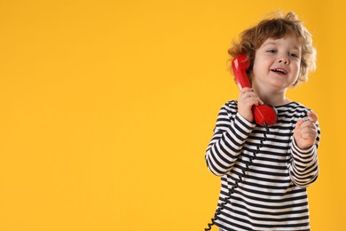 Photo of Cute little boy with telephone handset on orange background, space for text