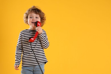 Photo of Cute little boy with telephone handset on orange background, space for text