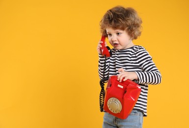 Photo of Cute little boy with telephone on orange background, space for text