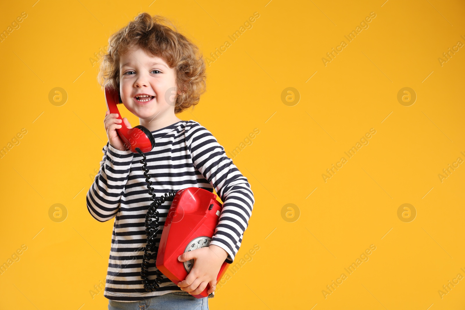 Photo of Cute little boy with telephone on orange background, space for text