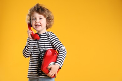 Photo of Cute little boy with telephone on orange background, space for text