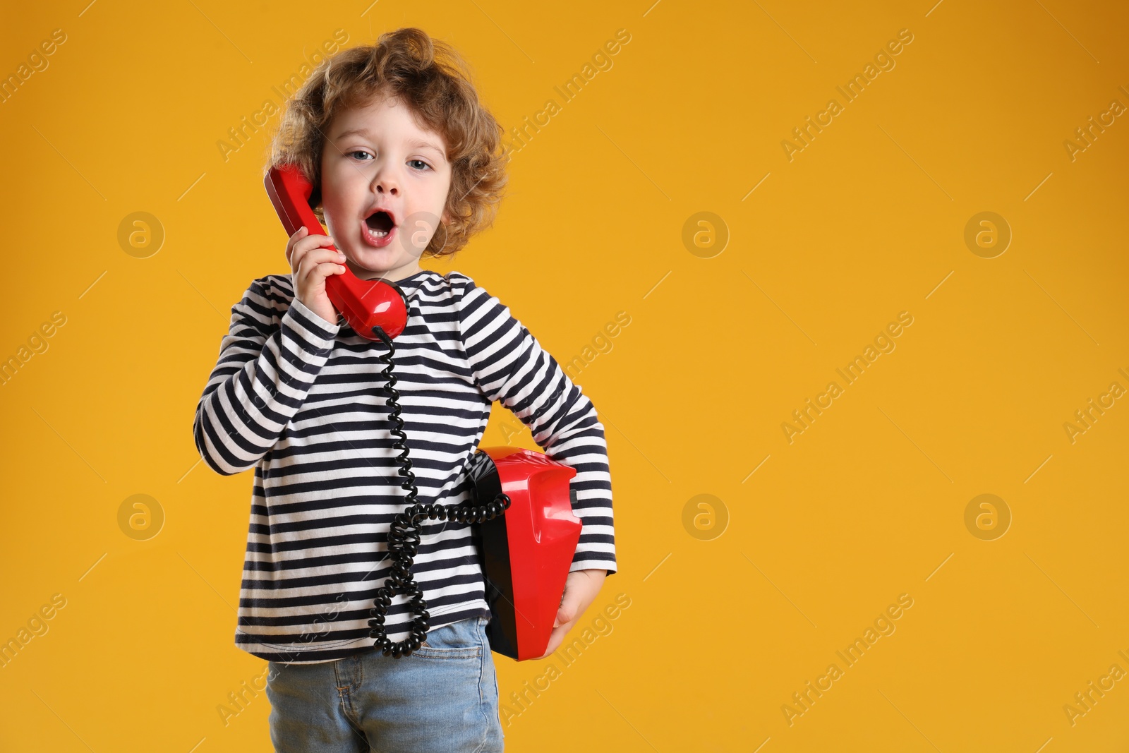 Photo of Cute little boy with telephone on orange background, space for text