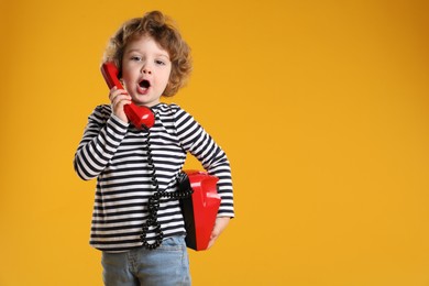 Photo of Cute little boy with telephone on orange background, space for text