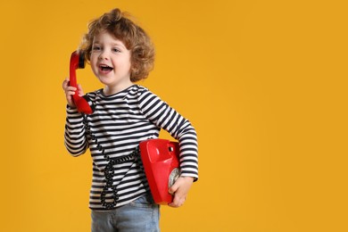 Photo of Cute little boy with telephone on orange background, space for text