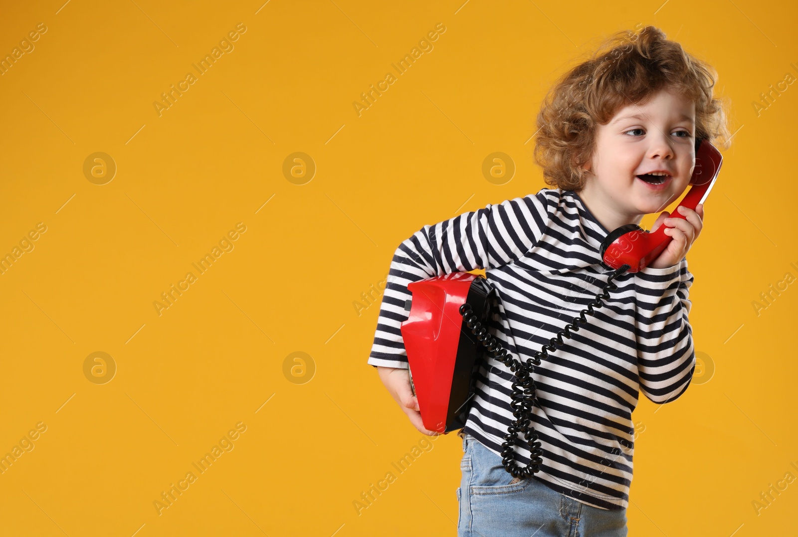 Photo of Cute little boy with telephone on orange background, space for text