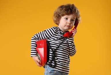 Photo of Cute little boy with telephone on orange background