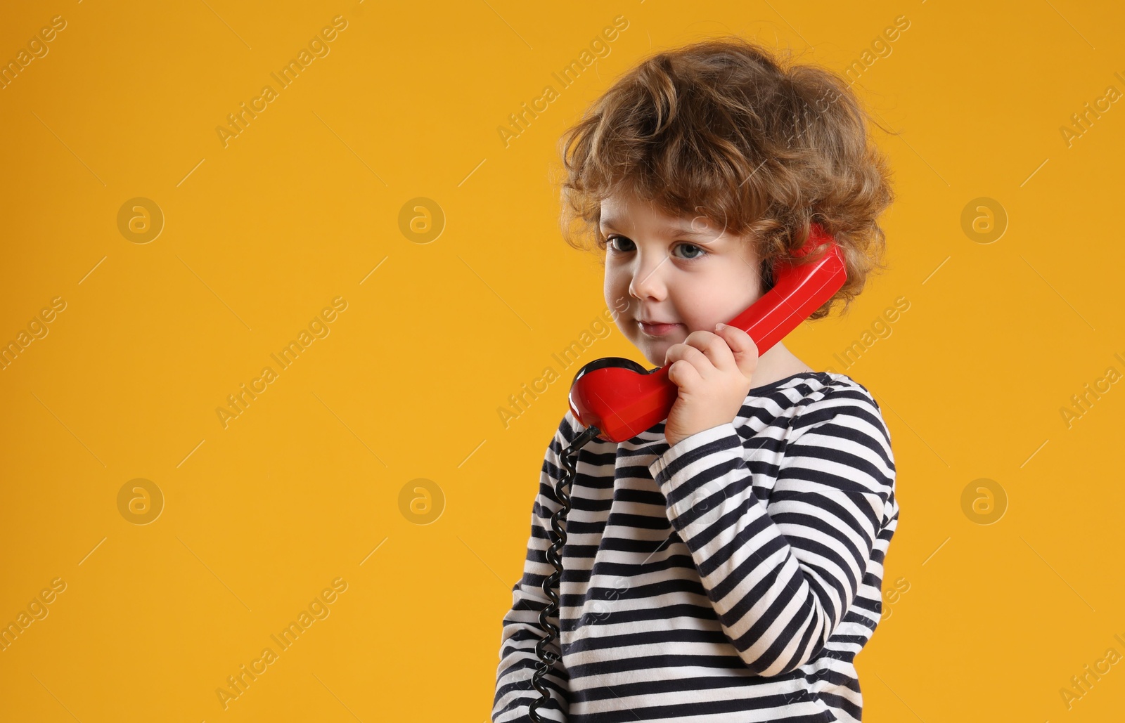 Photo of Cute little boy with telephone handset on orange background, space for text