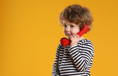 Photo of Cute little boy with telephone handset on orange background, space for text