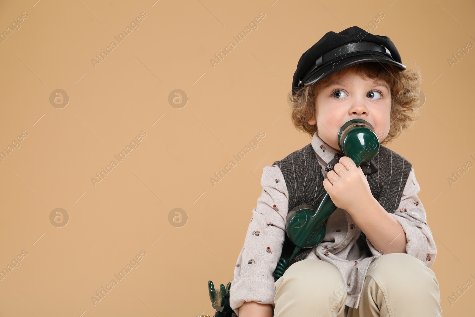 Photo of Cute little boy with old telephone on beige background, space for text