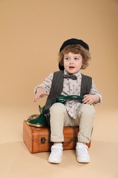 Photo of Cute little boy with old telephone and suitcase on beige background