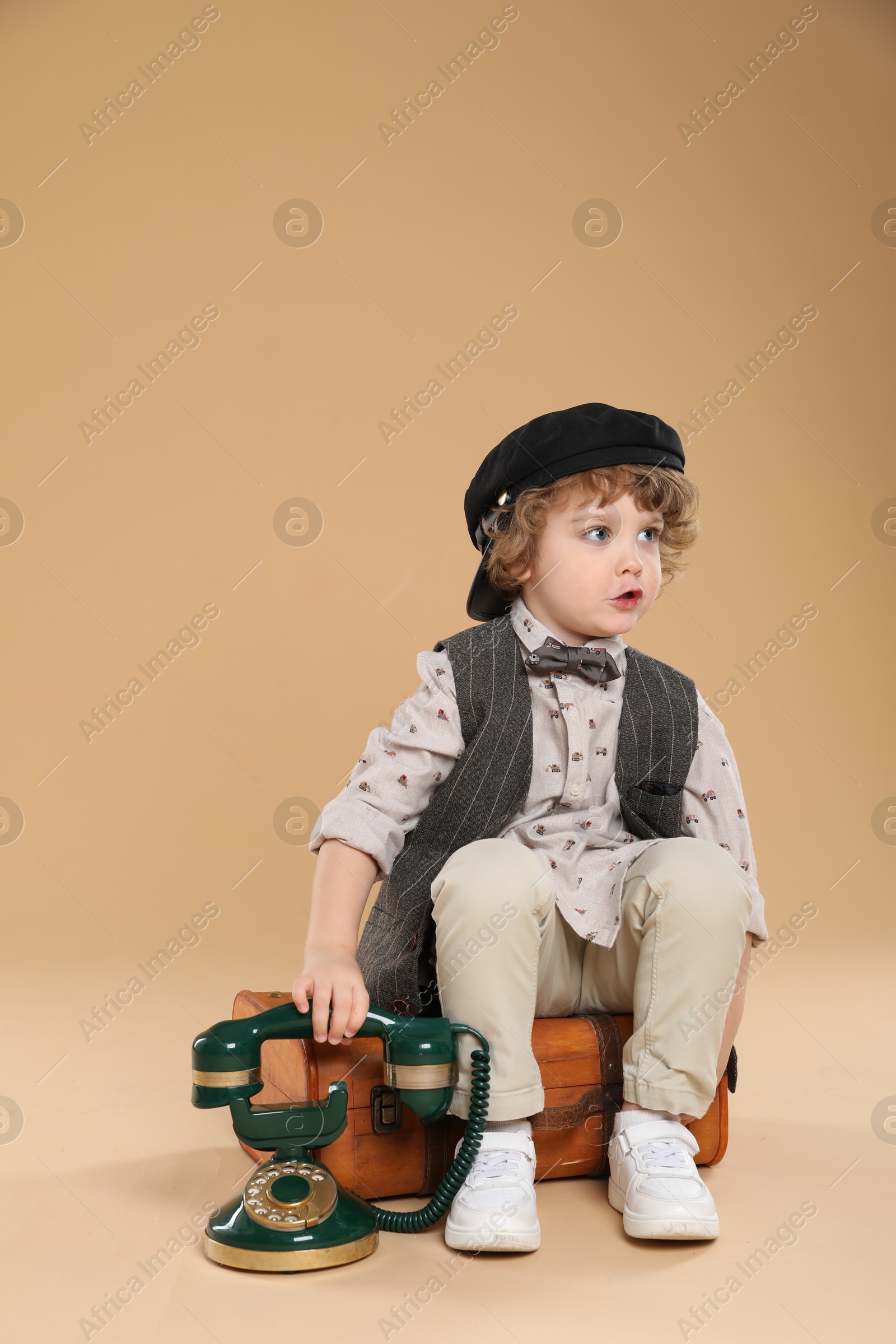 Photo of Cute little boy with old telephone and suitcase on beige background