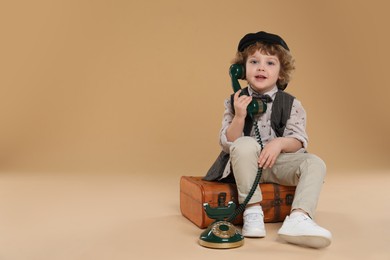 Photo of Cute little boy with old telephone and suitcase on beige background, space for text