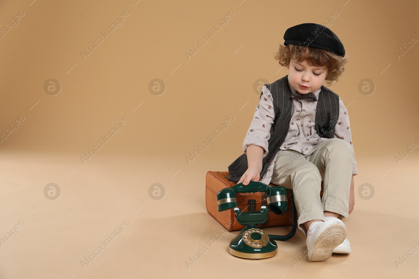 Photo of Cute little boy with old telephone and suitcase on beige background, space for text