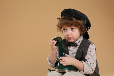 Photo of Cute little boy with old telephone on beige background, space for text