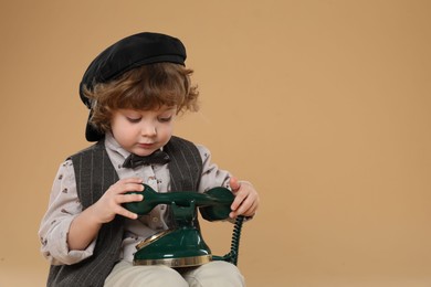 Photo of Cute little boy with old telephone on beige background, space for text