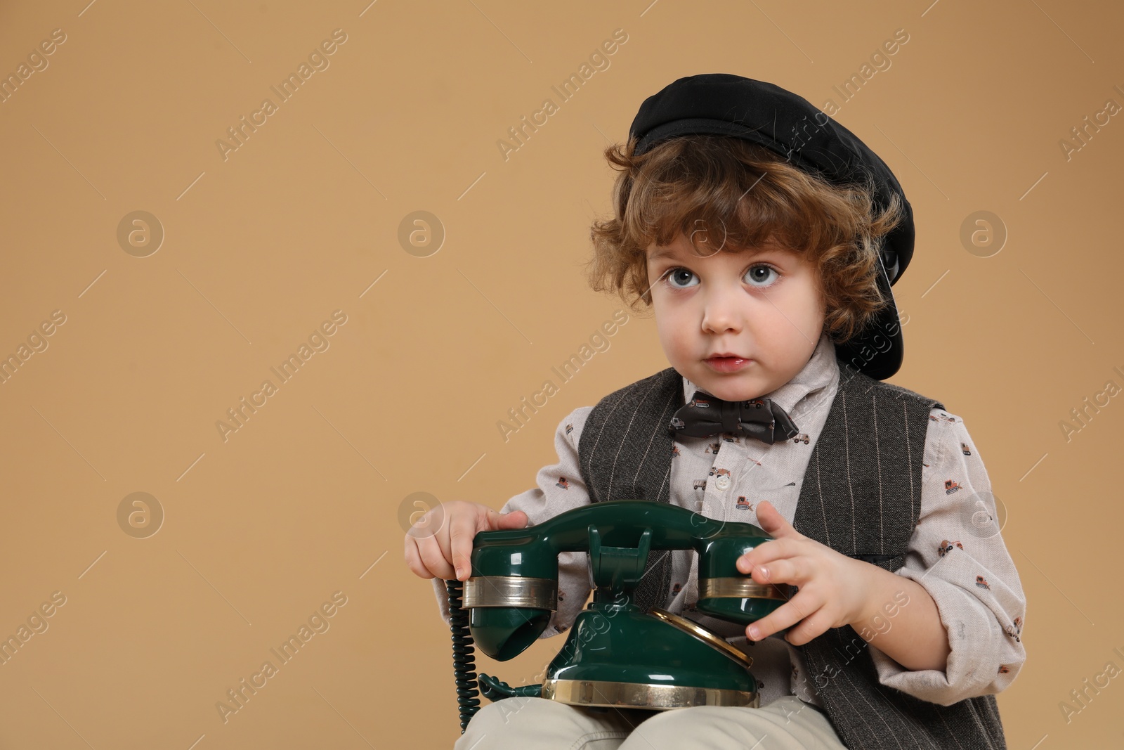 Photo of Cute little boy with old telephone on beige background, space for text