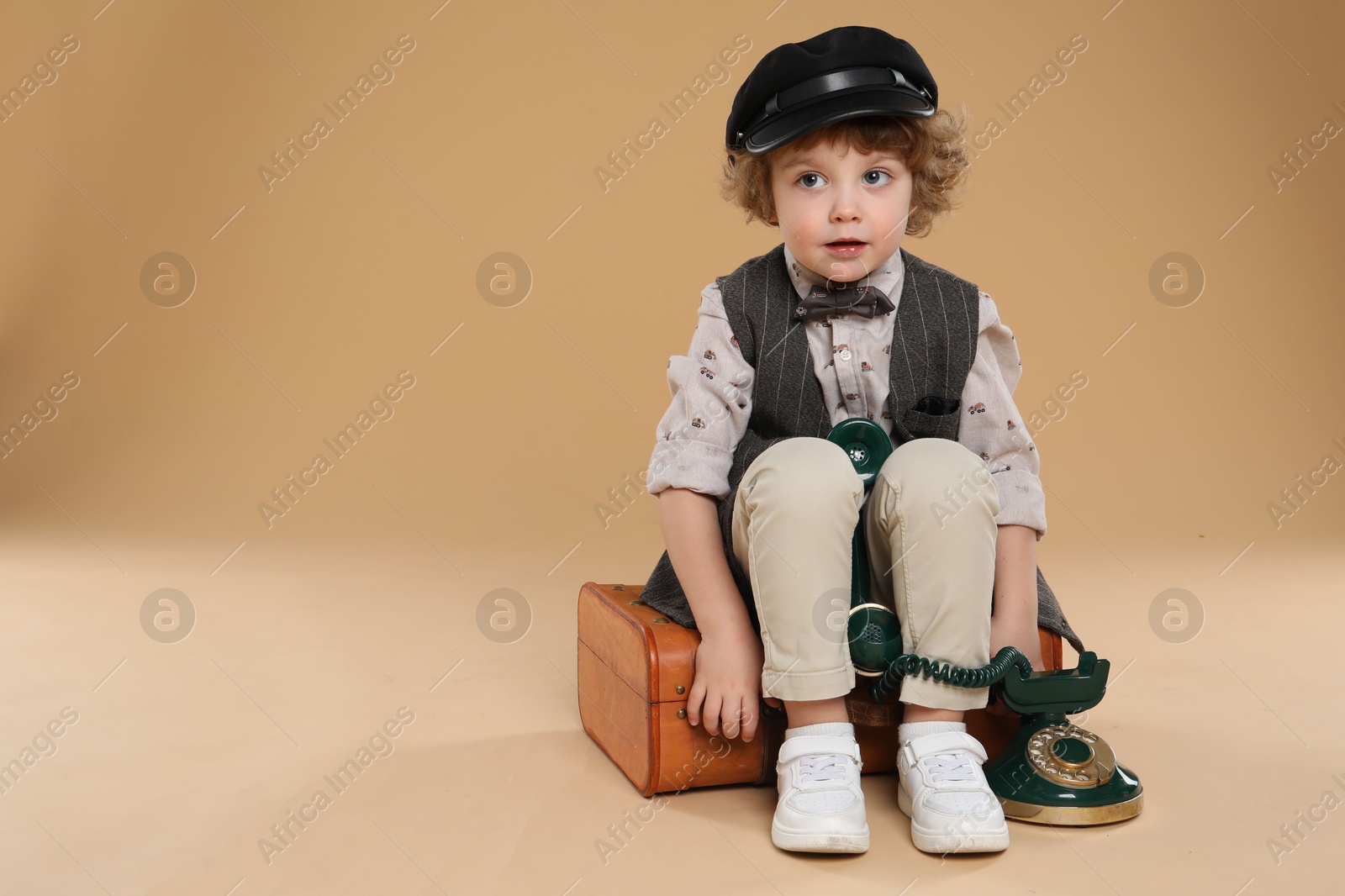 Photo of Cute little boy with old telephone and suitcase on beige background, space for text