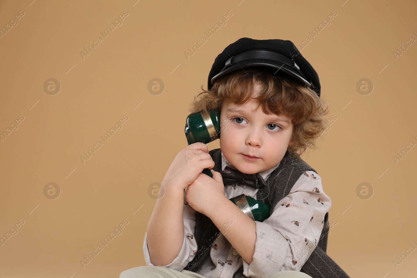 Photo of Cute little boy with telephone handset on beige background, space for text