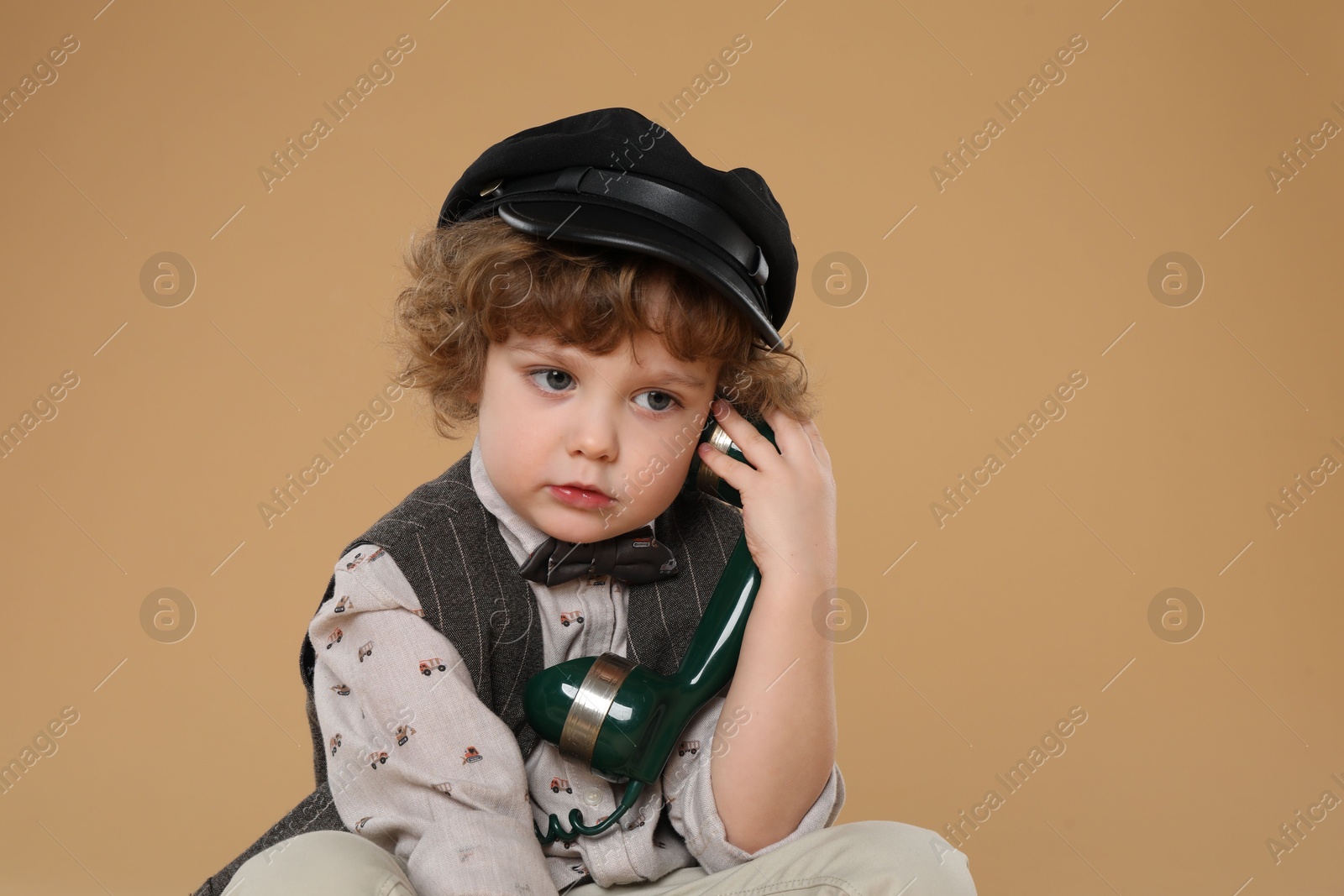 Photo of Cute little boy with telephone handset on beige background, space for text