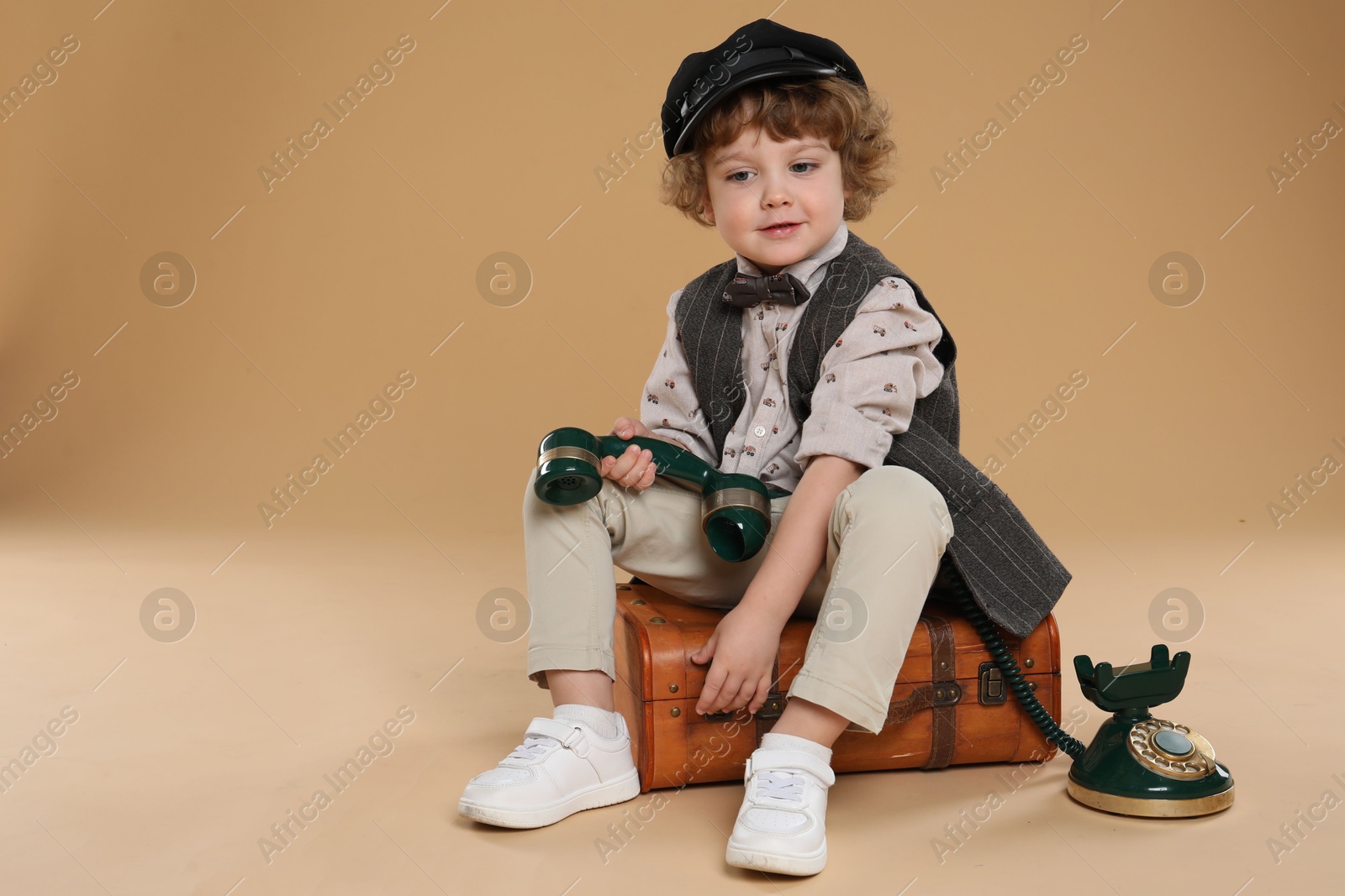 Photo of Cute little boy with old telephone and suitcase on beige background, space for text