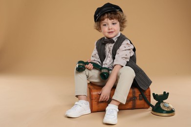 Photo of Cute little boy with old telephone and suitcase on beige background, space for text