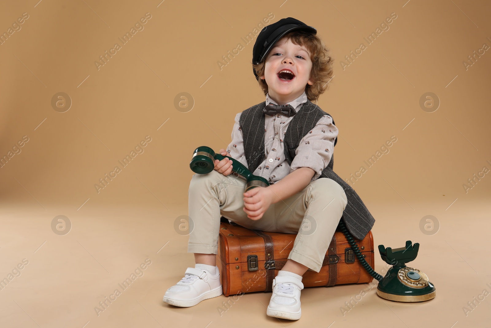 Photo of Cute little boy with old telephone and suitcase on beige background, space for text