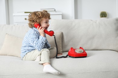 Photo of Cute little boy with telephone on sofa indoors