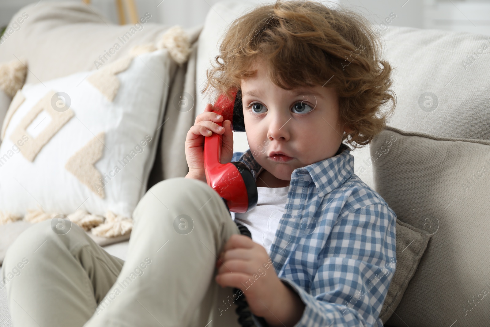 Photo of Cute little boy with telephone handset on sofa indoors