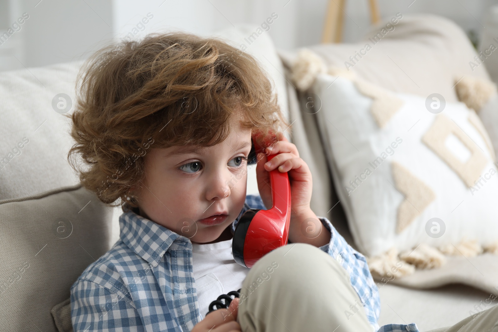 Photo of Cute little boy with telephone handset on sofa indoors, space for text