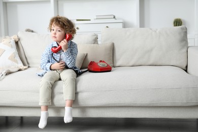 Photo of Cute little boy with telephone on sofa indoors