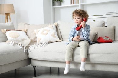 Photo of Cute little boy with telephone on sofa indoors