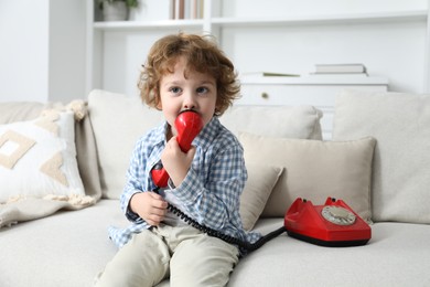 Photo of Cute little boy with telephone on sofa indoors