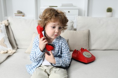 Photo of Cute little boy with telephone on sofa indoors