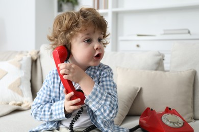 Photo of Cute little boy with telephone on sofa indoors