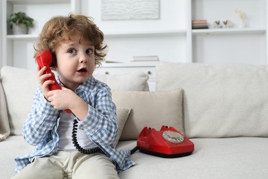 Photo of Cute little boy with telephone on sofa indoors